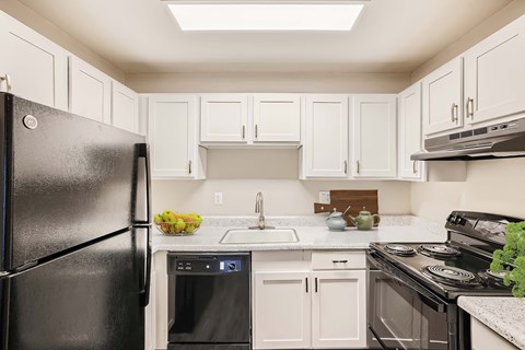 A black refrigerator stands in a kitchen with white cabinets and appliances.